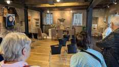 Besucher stehen in einem Ausstellungsraum vor einer Bühne mit Stühlen und Kunstwerken.