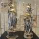 Zwei silberne Figuren von Königinnen mit Kronen und Zeptern in einem Museum.