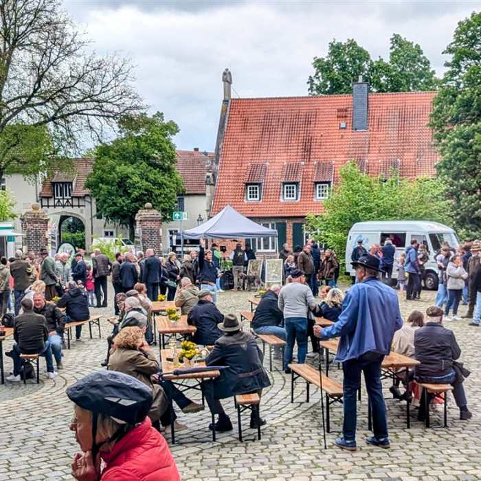 Menschen versammeln sich auf einem gepflasterten Hof vor einem historischen Gebäude, mit Essensständen und Sitzgelegenheiten.