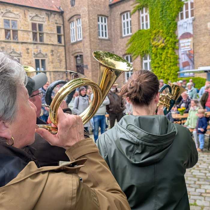 Personen spielen Hörner in einer Menschenmenge vor einem Gebäude.
